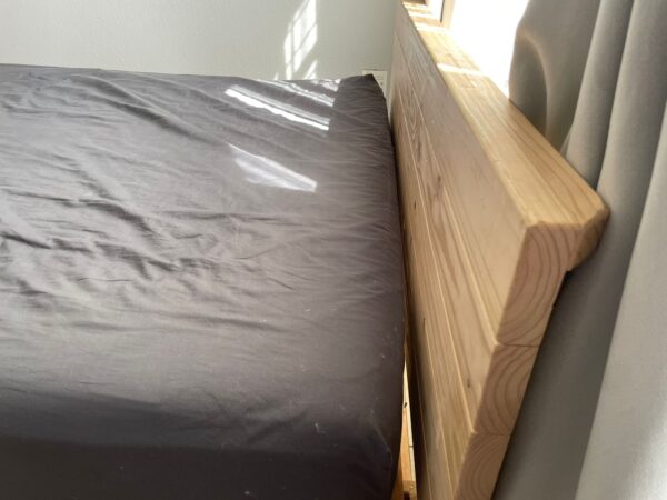 Wooden headboard against grey curtains with mattress and grey sheet