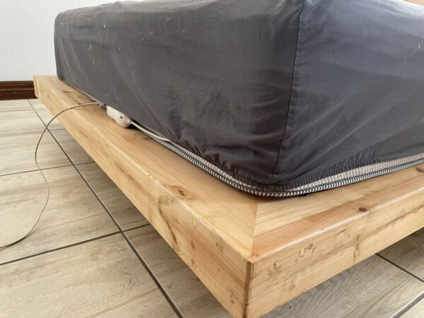 End of wooden floating bed with mattress an grey sheet