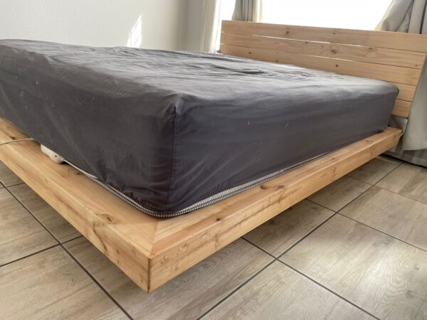 Wooden floating bed with mattress an grey sheet low angle