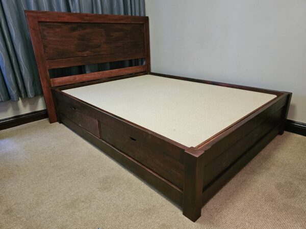 Dark stained wooden bed with headboard against blue curtains