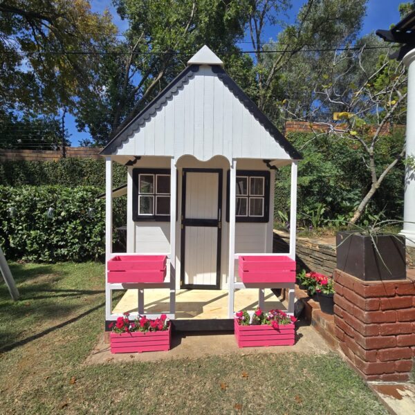 White and black wooden playhouse with pink flower crates front view