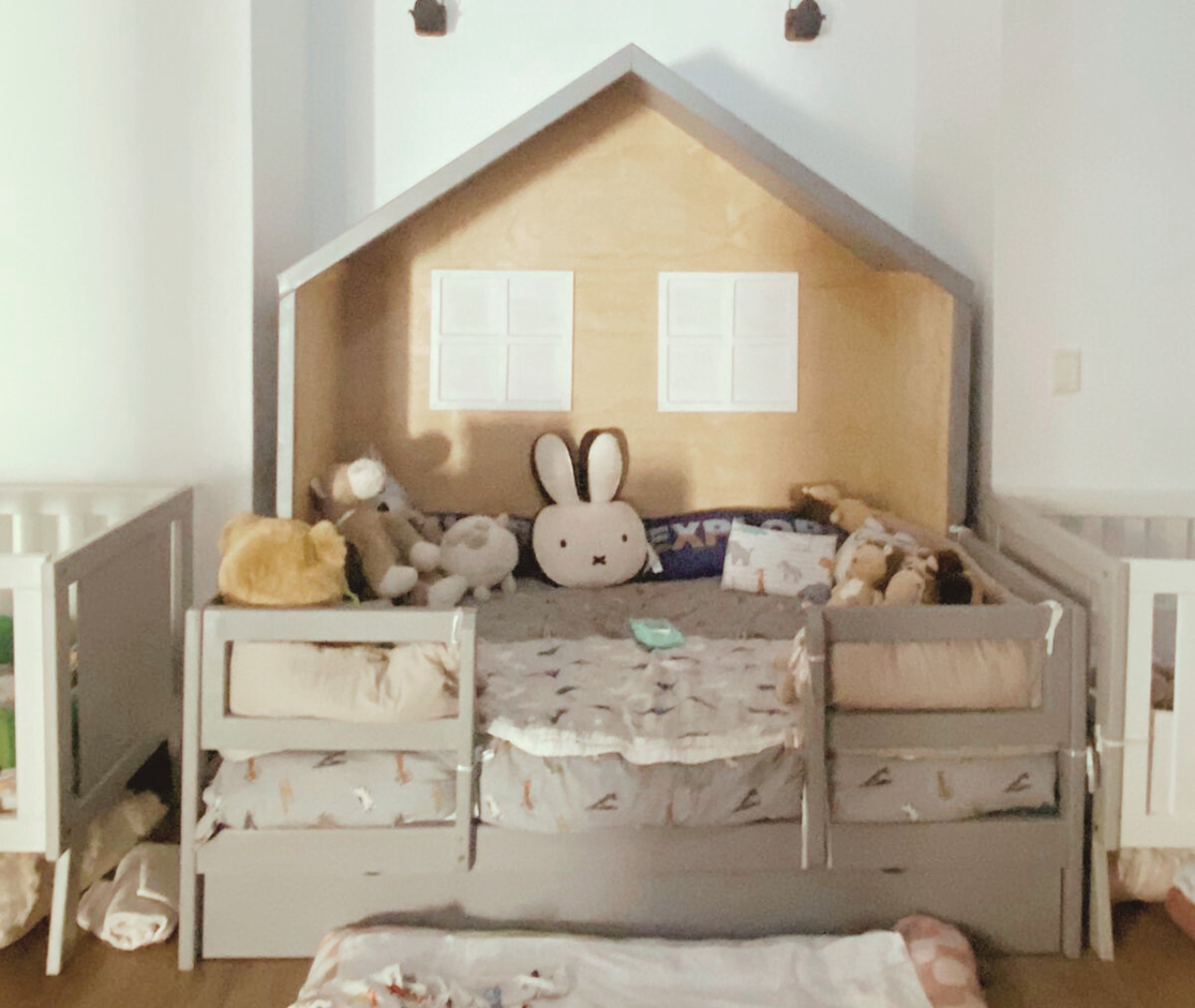 Grey kids bed house with plush toys on top and storage doors