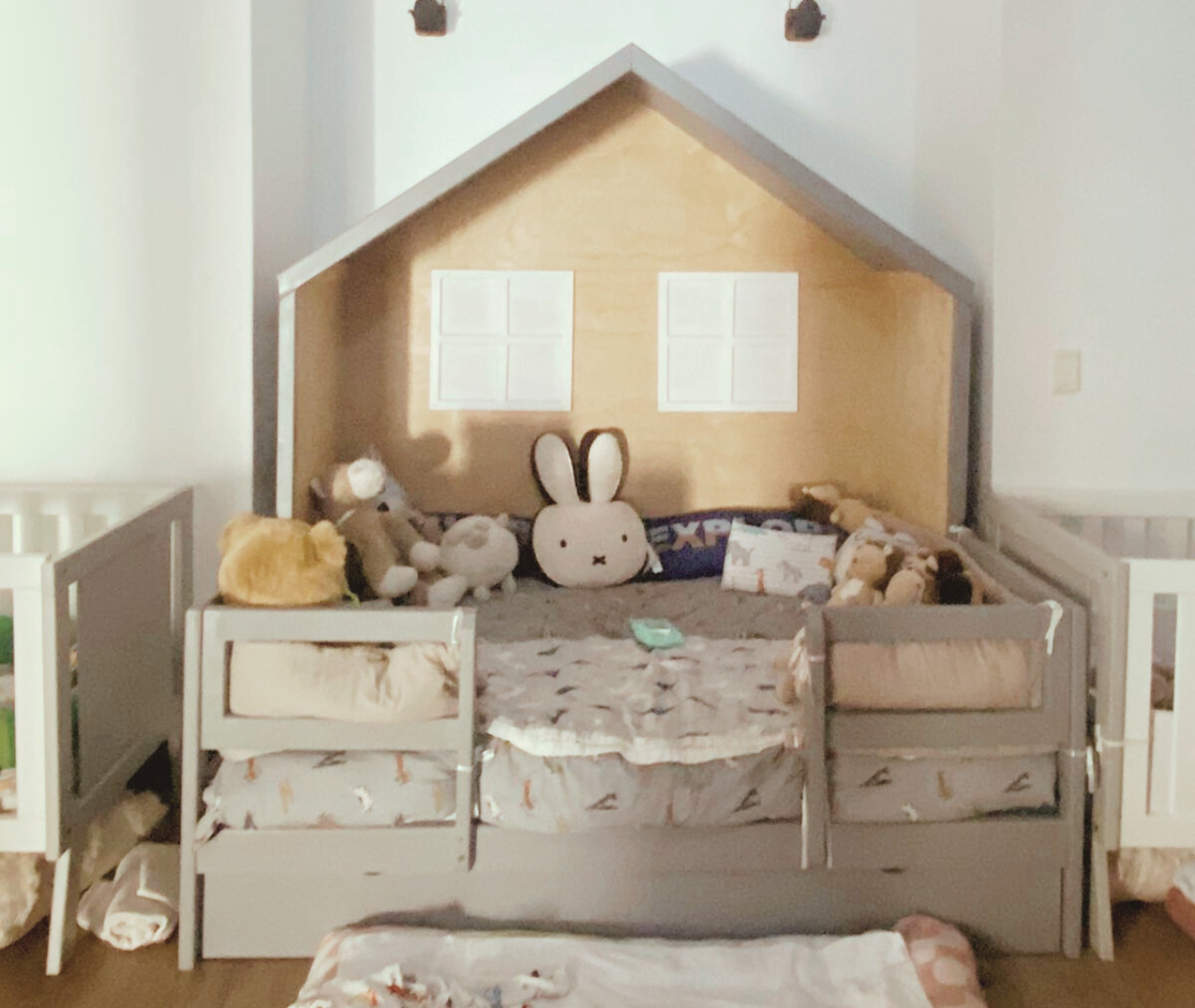 Grey kids house bed with plush toys on top